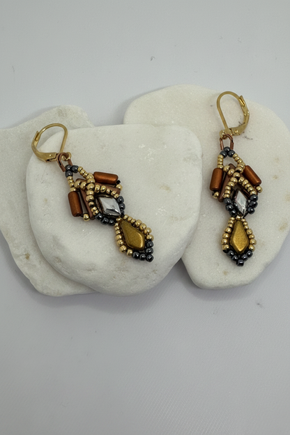 Pair of gold beaded earrings with copper, silver gold and gray beads on a white stone surface.