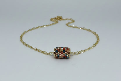 Gold necklace with a beaded woven pendant on a white background