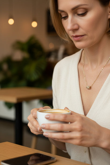 Woman wearing a gold necklace with a pendant in a light gray sweater.