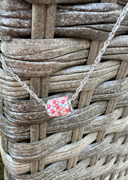 Silver necklace with a colorful beaded pendant on a woven surface