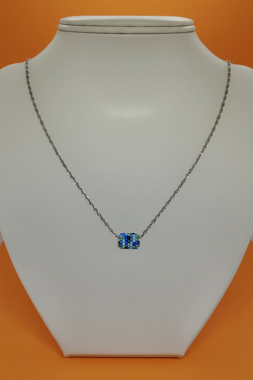 Silver necklace with a beaded woven pendant on a white bust with an orange background