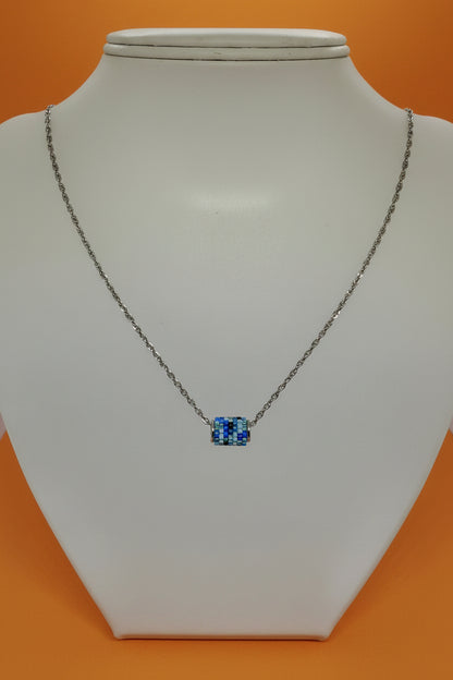 Silver necklace with a beaded woven pendant on a white bust with an orange background