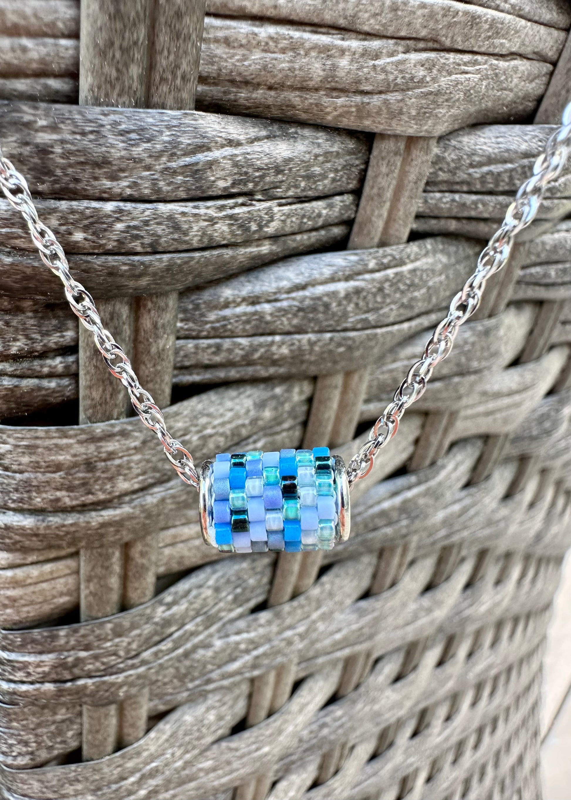 Silver necklace with a colorful beaded pendant on a woven surface