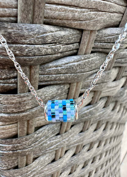 Silver necklace with a colorful beaded pendant on a woven surface