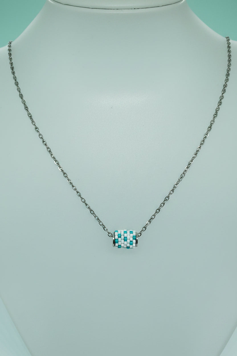 Silver necklace with a beaded woven pendant on a teal background