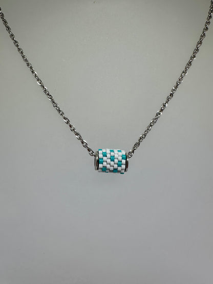 Close up of silver necklace with a beaded woven pendant with white and teal beads on a white bust 