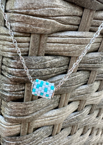 Silver necklace with a colorful beaded pendant on a woven surface