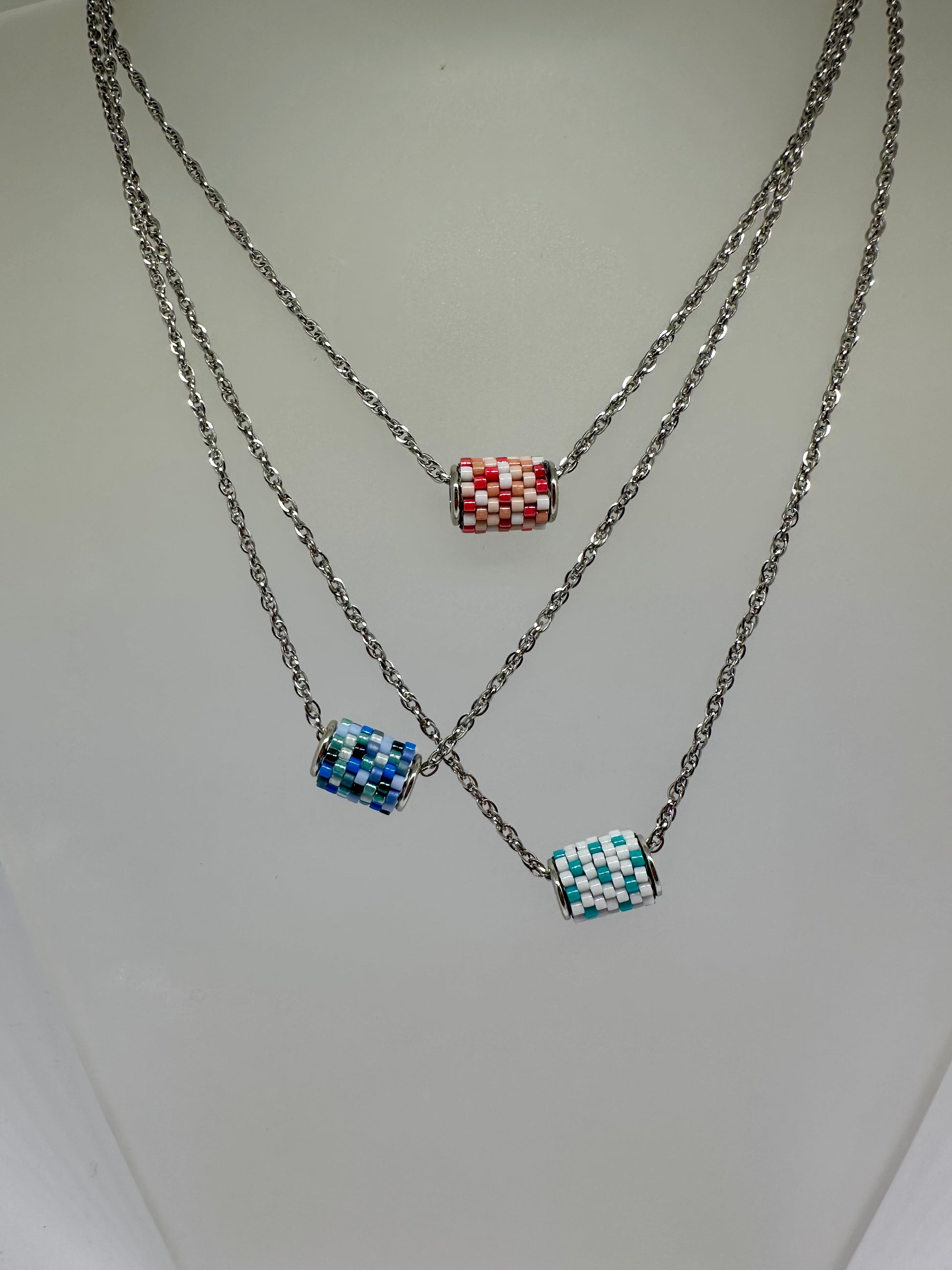 Three necklaces with colorful beaded pendants on a light gray background