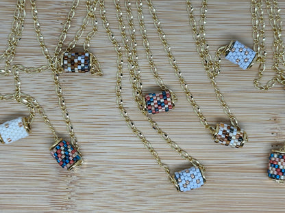 Gold necklaces with beaded barrel pendants on a woven surface.
