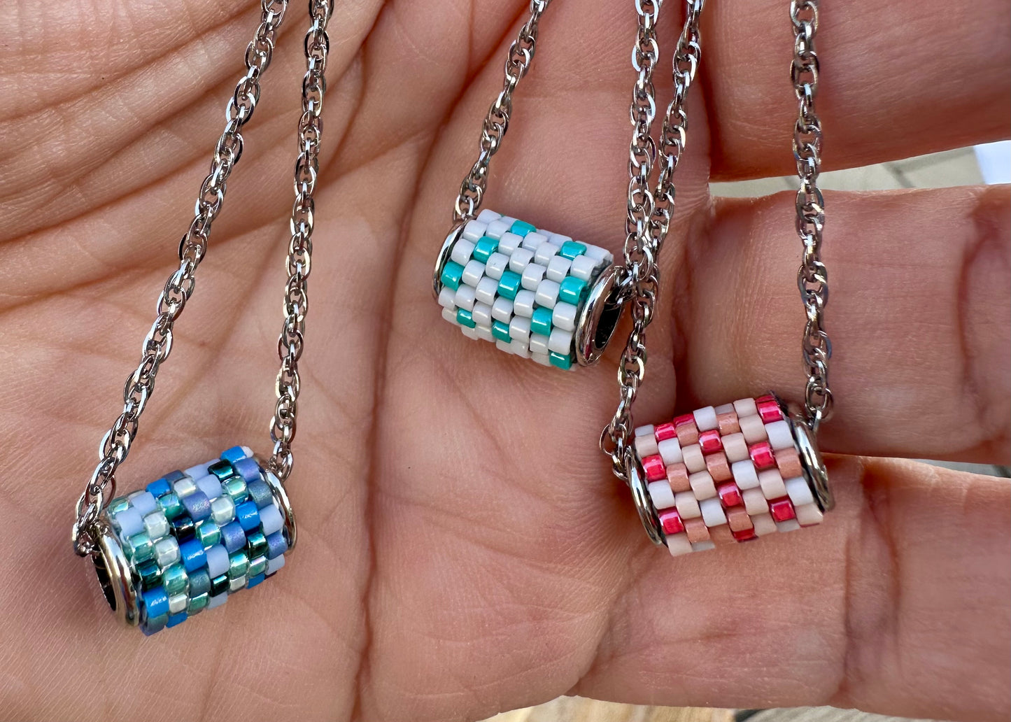 Three beaded pendants on chains held in a hand