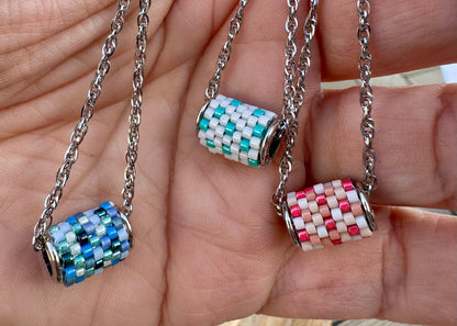 Three beaded pendants on chains held in a hand