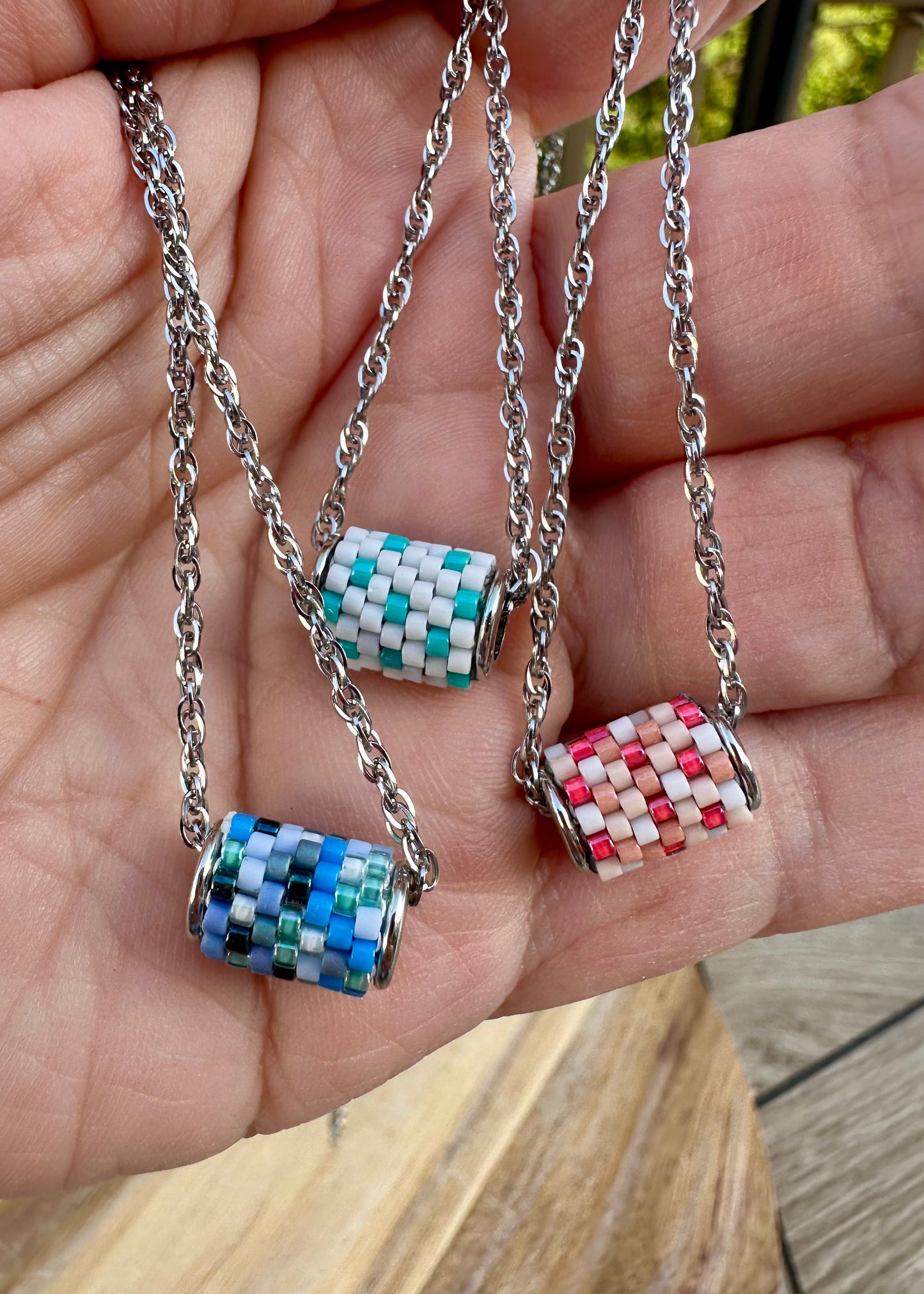 Three colorful barrel-shaped pendants on silver chains held in a hand.