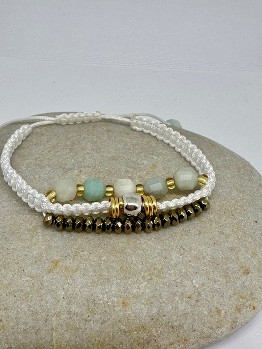 Beaded macrame bracelet with gemstones, gold beads, a silver accent bead, and bronze-colored beads on a stone surface.