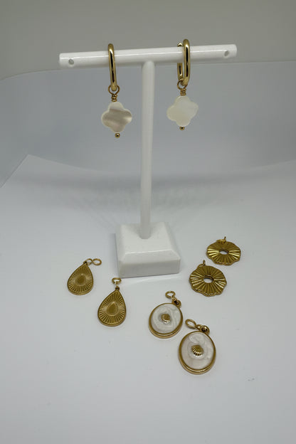 Gold huggie earrings with white mother of pearl clover charms surrounded by interchangeable charms in gold and white on a white stand and surface.