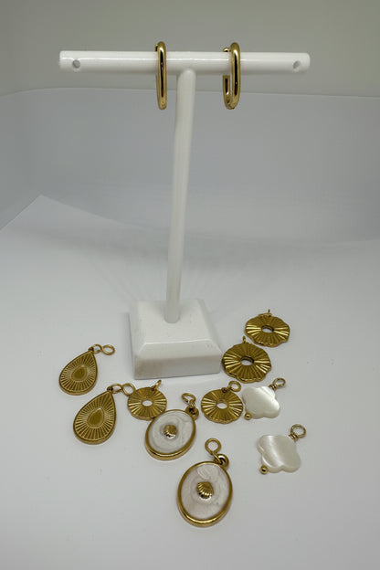 Gold and white huggie earrings with interchangeable pieces on a white stand against a white background