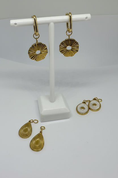 Gold huggie earrings with gold starbursts surrounded by interchangeable charms in gold and white on a white stand and surface.