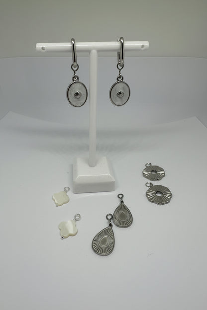 Silver huggie earrings with white shell charms surrounded by interchangeable charms in silver and white on a white stand and surface.